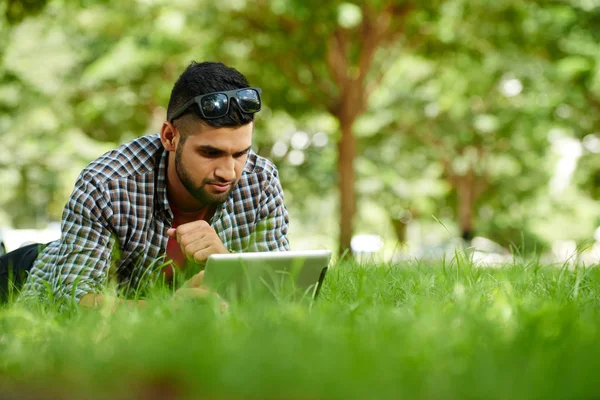 Fundersam Indisk Ung Man Liggande Gräset Och Läsa Nyheter Den — Stockfoto