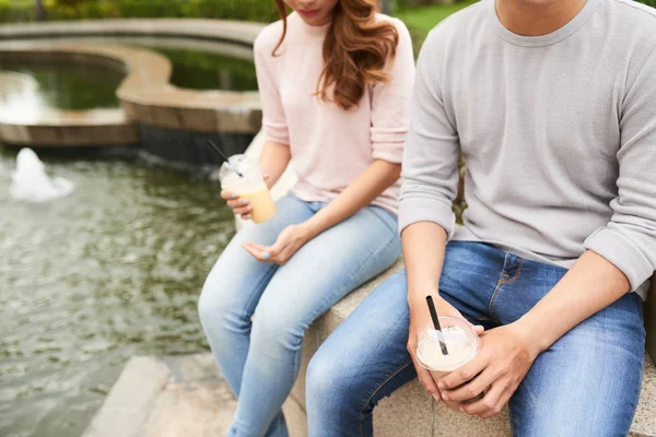 噴水のそばに座って ミルク カクテルを楽しんでいるカップルのトリミングされた画像 — ストック写真