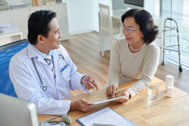 Dijital tablet elinde tutan ve Asya hastaya test sonuçlarını gösteren doktor