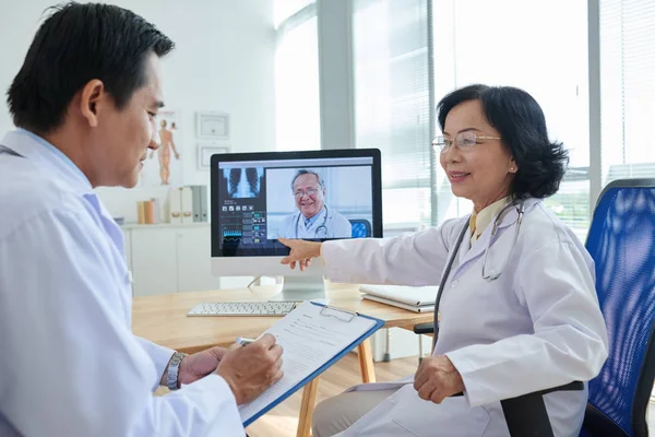 Group of experienced physicians gathered together in office and having video conference meeting