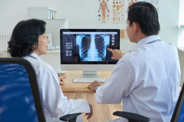 自信的医生坐在电脑前检查胸部 其中一人指着屏幕上的东西 — 图库照片