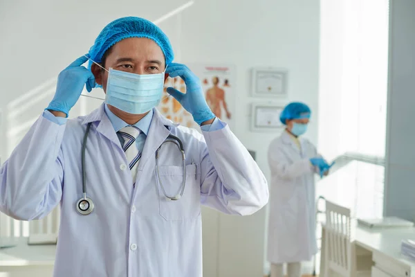 越南外科医生的腰部画像在手术前戴上医疗口罩 他的同事站在他身后 — 图库照片