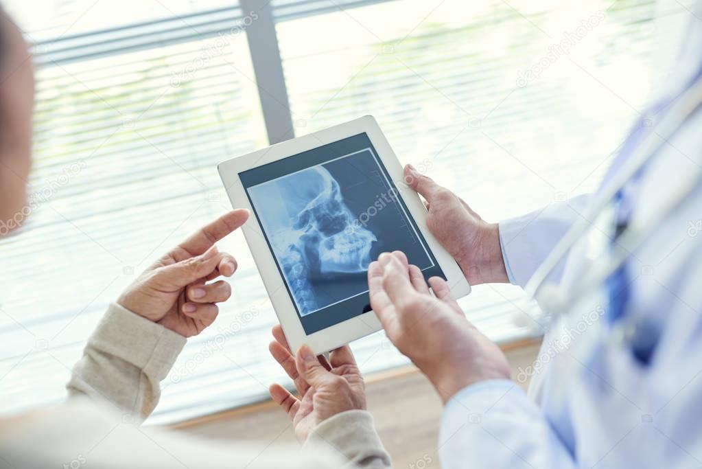 dentist showing dental X-ray to patient with help of digital tablet 