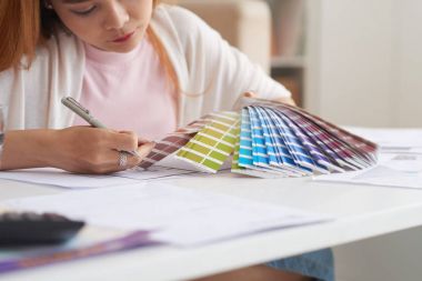 Closeup portrait of young Asian woman working with floor plans and color swatches choosing interior design for new house