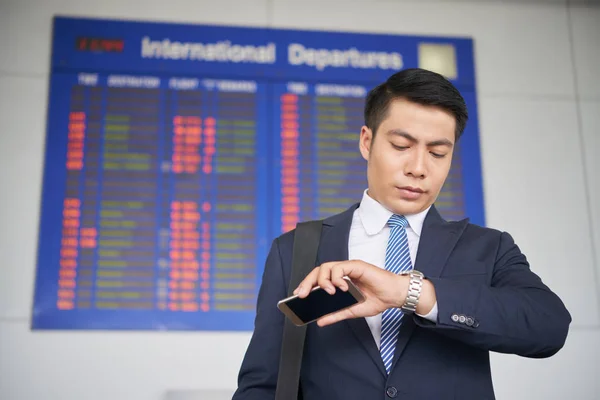 アジア系のビジネスマンが空港に彼の飛行を待っている間の腕時計で時間をチェック — ストック写真
