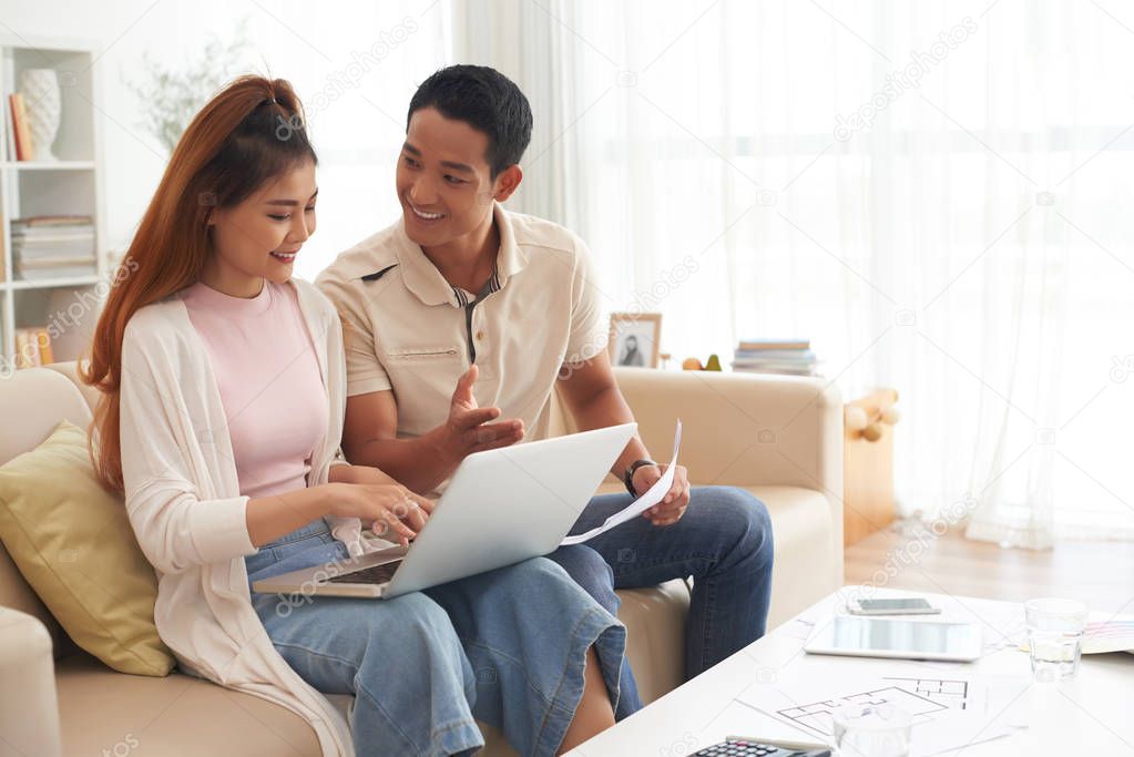 Portrait of cheerful Asian couple discussing purchase of new house, looking for real estate property online