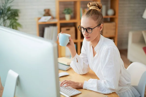 手里拿着一杯咖啡的女人在电脑上工作 — 图库照片