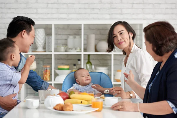 男の子の赤ちゃんと大きな家族の朝食のテーブルに座って若いアジア女性の肖像画 — ストック写真