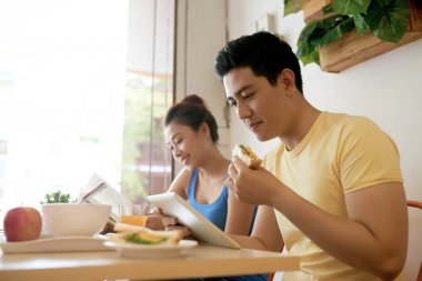 Genç Vietnamlı karı koca kahvaltı yapıyor ve kitap okuma