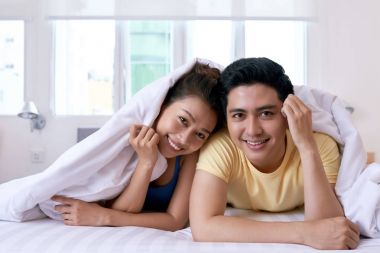 Gülümseyen güzel Vietnamca çift yatakta kameraya bakarak yalan