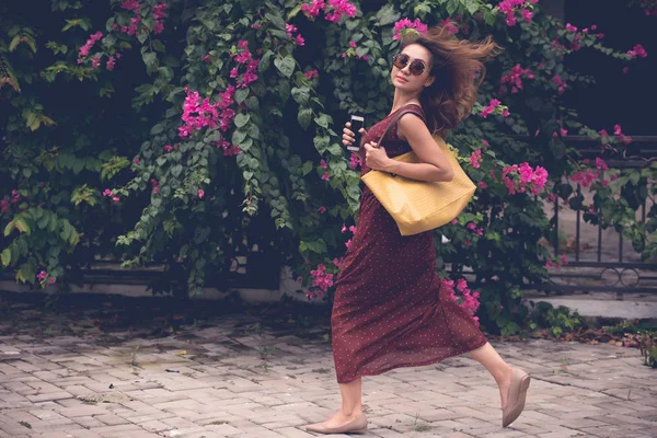 Beautiful young woman with big purse and smartphone running in the park