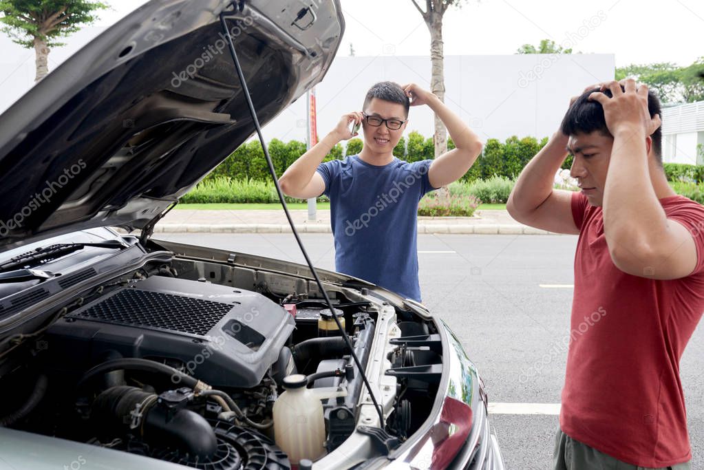 shocked Asian men looking under hood of car in order to find cause of breakage 