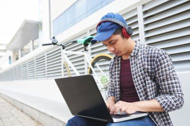 Genç adam açık havada otururken programlama kulaklık