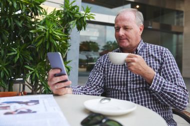 Sabah kahve içer ve smartphone cep telefonu ile haber okuma olgun adam