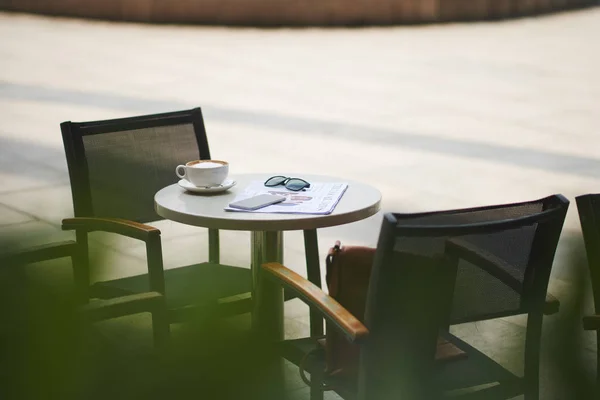 新聞とそれをカプチーノのカップを持つカフェ テーブル — ストック写真