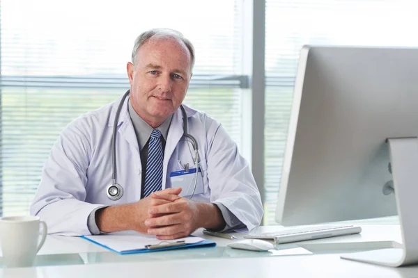 Portrait of aged medical worker sitting at his workplace and smiling at camera