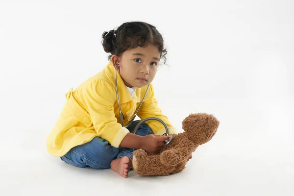 可爱的小女孩玩医生 听她的泰迪熊与听诊器 孤立的白色背景 — 图库照片