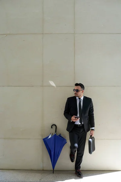 携帯電話 スーツ ケースと壁を建物に立っているビジネスマン — ストック写真