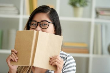 Bir kitapla yüzünü kaplayan gözlük ile akıllı kız portresi