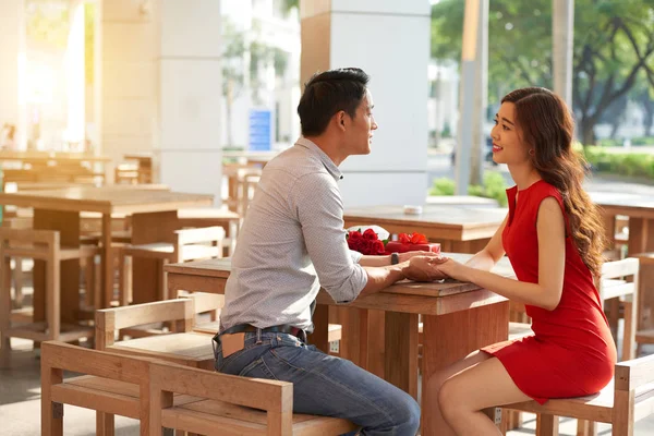 魅力的な若い女性は赤いドレスを着て 彼女の手を優しく握って彼氏とカフェに座って — ストック写真