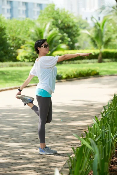 ウォーミング アップやトレーニングを晴れた日に公園でジョギング中に足をストレッチ陽気なアジアの女性の肖像画 — ストック写真