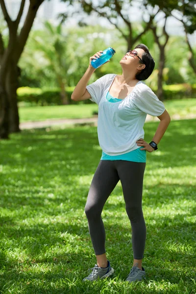 Portrait of healthy Asian woman drinking water during  workout in park on sunny day