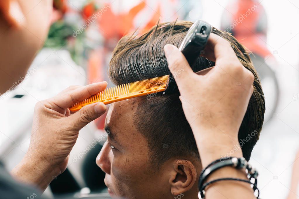 Hairstylist doing fashionable haircut for male client, barber cutting hair with electric trimmer