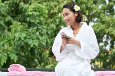 Genç Asyalı kadın ile açık havada dinlenme spa işlemden sonra smartphone