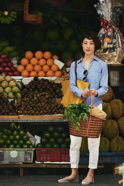 Pretty Japanese woman standing at stall with fresh exotic fruits