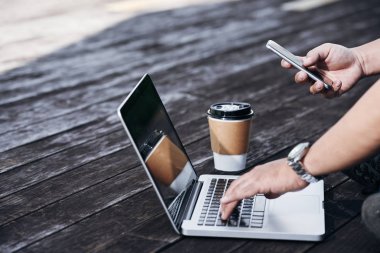 Eller üstünde laptop çalışma ve smartphone kontrol freelancer