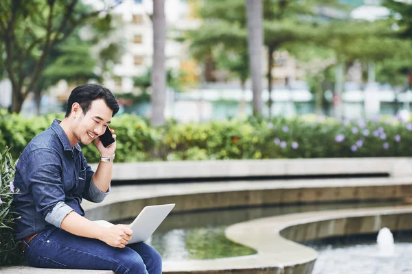 Cheerful young businessman calling on the phone and reading information on digital tablet