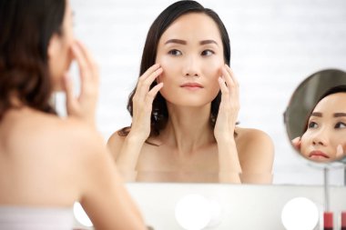 Çinli genç kadın yüz kremini uygularken aynaya bakıyor