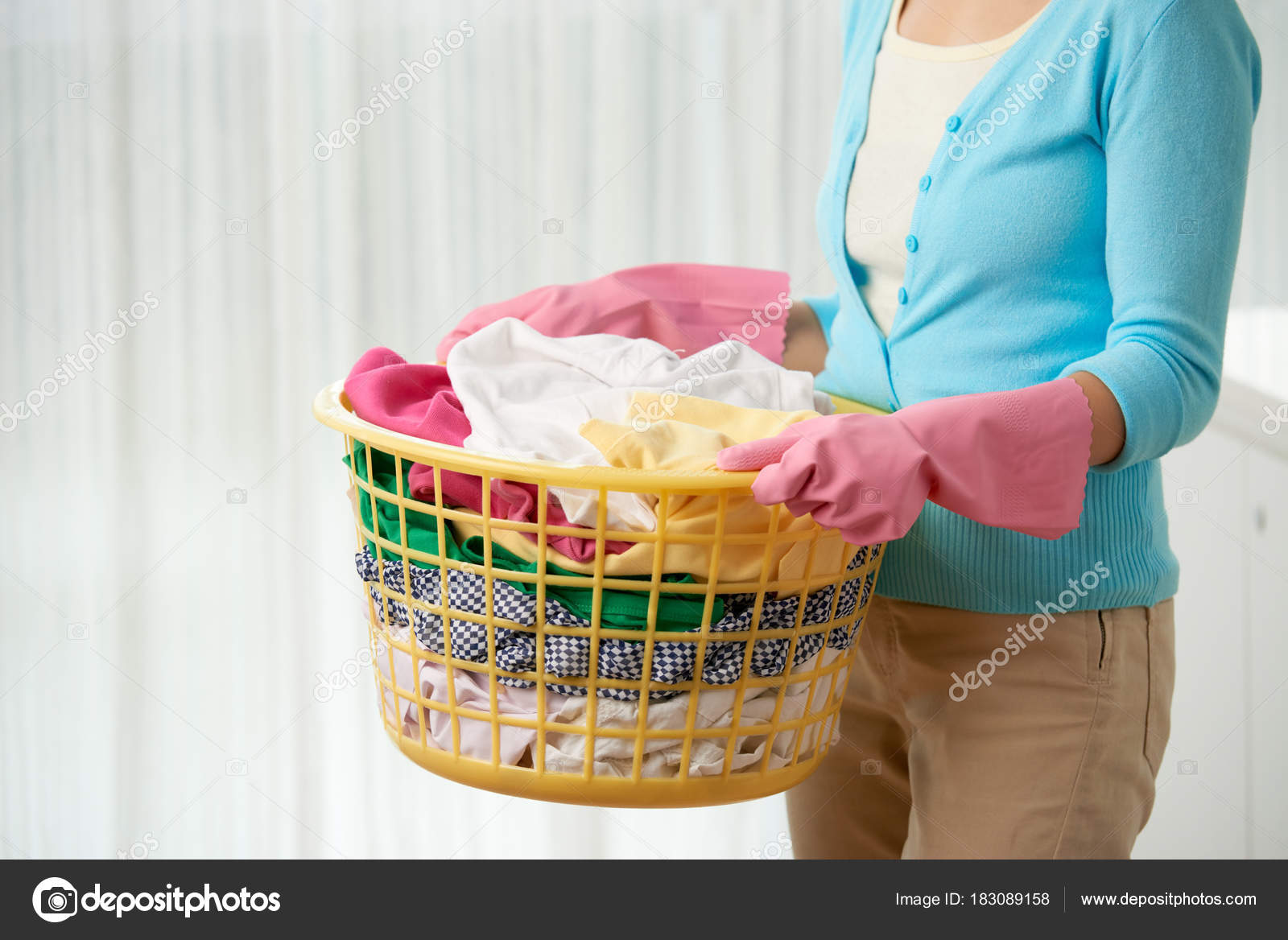 Ama de casa joven con ropa y guantes de goma en cesta, cerca de arriba
