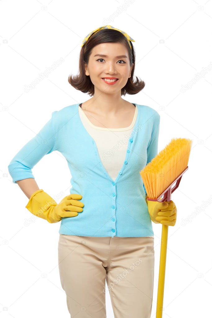 Attractive young housekeeper wearing rubber gloves with broom in hands and posing