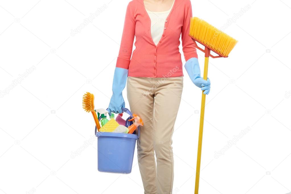 Unrecognizable housekeeper in rubber gloves holding broom and bucket with cleaning utensils in hands while standing against white background
