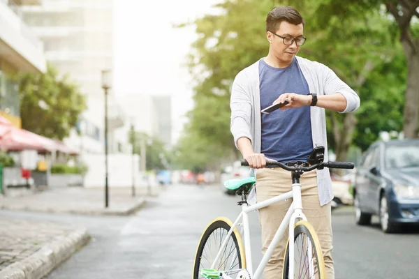 Cyclist standing under rain and checking time