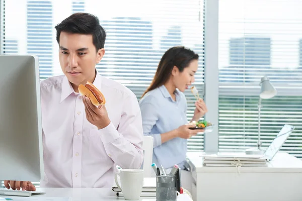 Concentrated Asian Manager Working Computer Eating Hot Dog While His — Stock Photo, Image