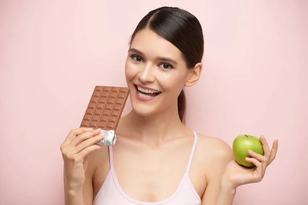 微笑的少妇在巧克力和绿色苹果之间选择 — 图库照片