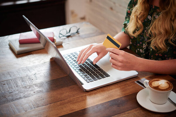 woman using laptop at table in coffee shop, holding credit card 