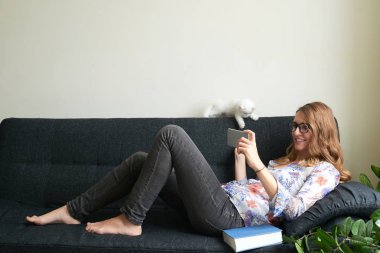 Smartphone cep telefonu ile bir şey izlemek ve kedi ile oynarken oldukça genç kadın