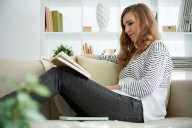 Kanepede oturan ve bir kitap okuma genç kadın