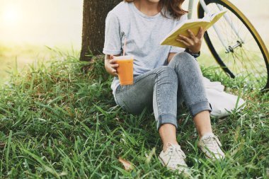 Kız öğrenci içme görüntüsünü kokteyl kırpılmış ve parkta bir kitap okuma