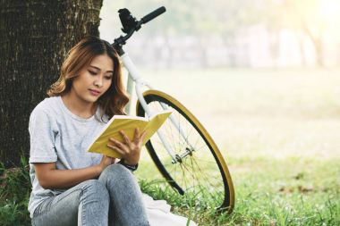 Ağacın altında oturan ve ilginç bir kitap okuma oldukça Vietnam genç kadın