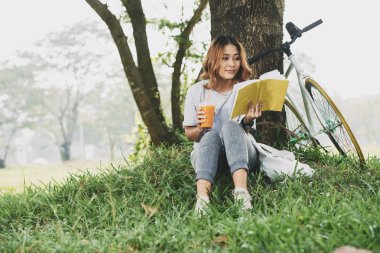 Lovely Asian young woman enjoying reading a book in the park clipart