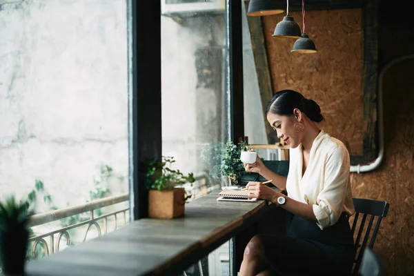 Hübsche Lächelnde Geschäftsfrau Die Kaffee Trinkt Und Ihren Tagesplaner Überprüft — Stockfoto