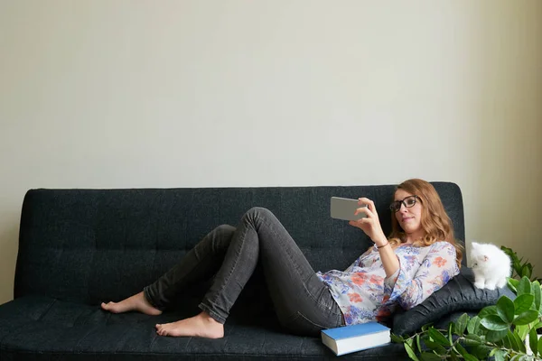 Mujer Bonita Gafas Descansando Sofá Viendo Videos Teléfono Inteligente — Foto de Stock