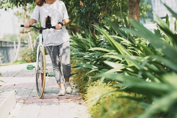 公園で彼女の自転車と一緒に歩いている若い女性 — ストック写真