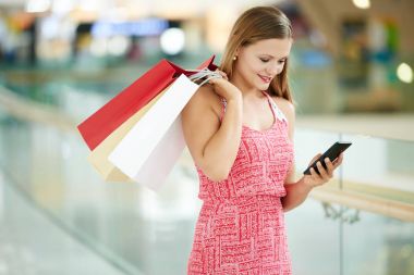 Çok gülümseyen kadın alışveriş torbaları onun smartphone cep telefonu ile mesaj okuma ile