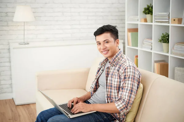 Asiático Homem Olhando Para Câmera Usando Laptop Enquanto Sentado Sofá — Fotografia de Stock