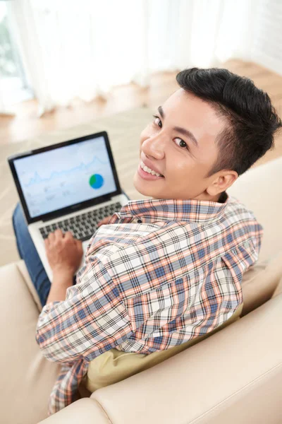 Asiático Hombre Mirando Cámara Usando Portátil Mientras Sentado Sofá Casa —  Fotos de Stock